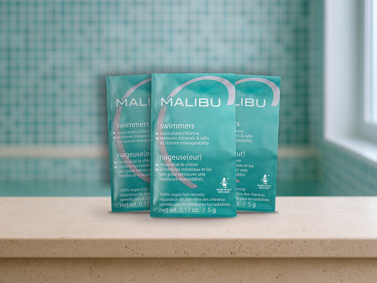 Malibu C Swimmers Wellness Remedy packets standing on a travertine spa ledge in front of aqua mosaic tile, product clearly in focus