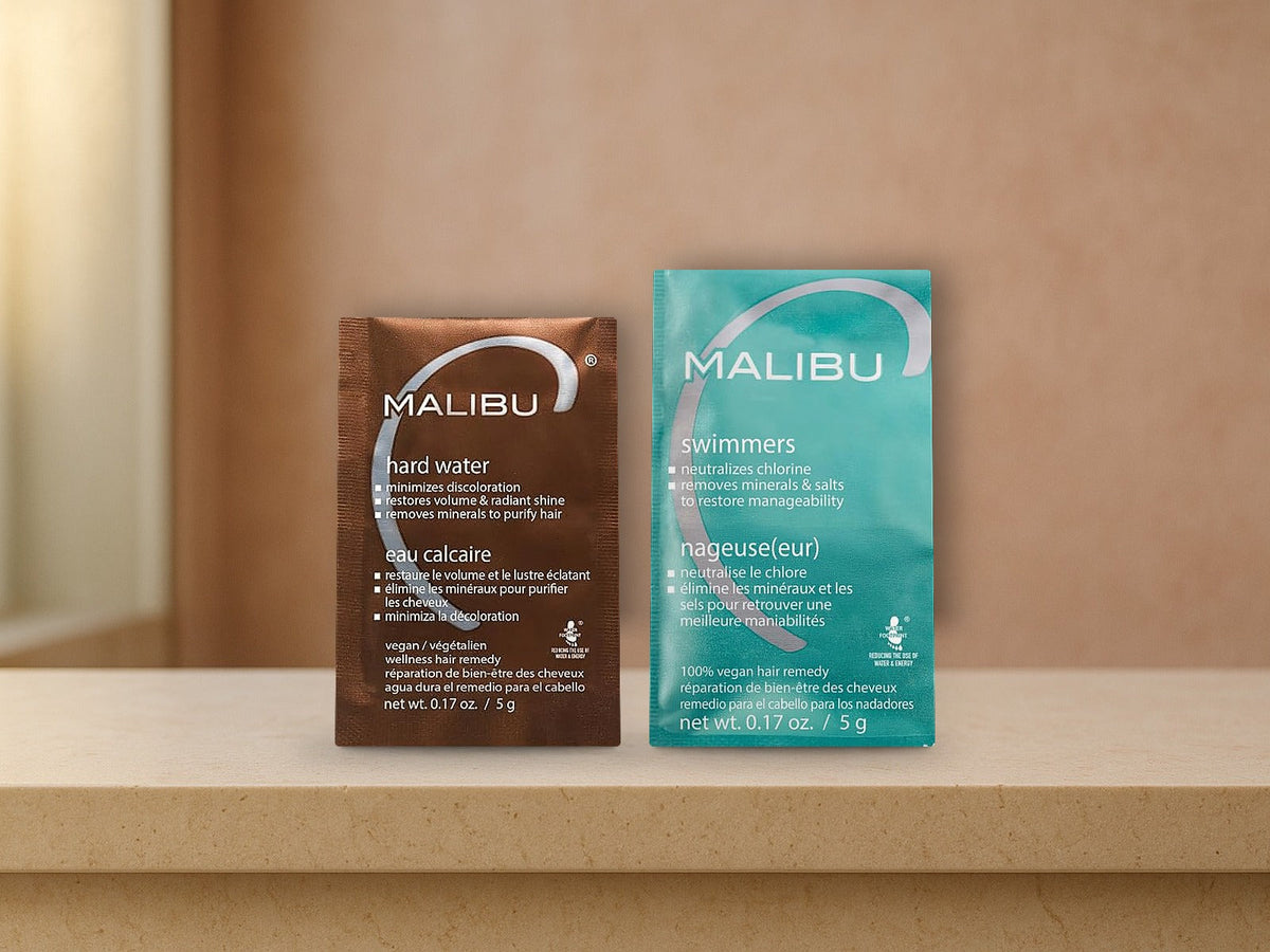 Malibu C Hard Water Wellness Remedy and Swimmers Wellness Remedy packets standing on a cream limestone ledge in front of a warm terracotta plaster wall, products clearly in focus