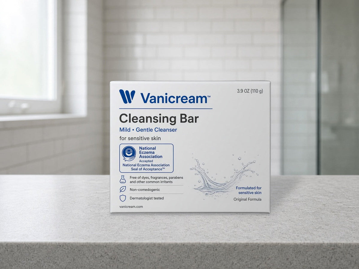 A white Vanicream Cleansing Bar box standing upright on a pale grey stone bathroom counter, with a white subway tile wall, a bright frosted window at left, and a glass shower door softly blurred at right