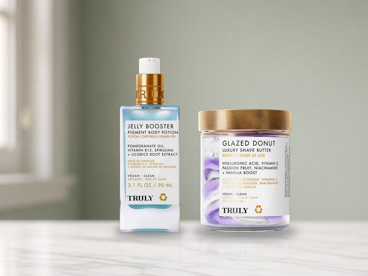 TRULY Jelly Booster Pigment Body Potion bottle and Glazed Donut Luxury Shave Butter jar on a white marble bathroom vanity in soft daylight.